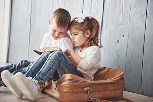 listo para grandes viajes. feliz niña y niño leyendo un libro interesante con un maletín grande. concepto de libertad e imaginación foto