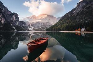 Gorgeous landscape. Wooden boat on the crystal lake with majestic mountain behind. Reflection in the water. Chapel is on the right coast