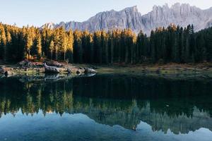 Moment of sunset. Autumn landscape with clear lake, fir forest and majestic mountains photo