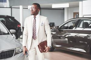 Young black businessman on auto salon background. Car sale and rent concept photo