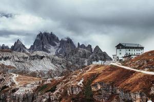 Tourists far away outside the home. Building standing high on the mountains near the bunch of cliffs with mist and clouds photo