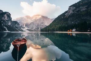 Wooden boat on the crystal lake with majestic mountain behind. Reflection in the water. Chapel is on the right coast photo