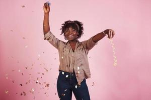 feliz como un niño. lanzando el confeti al aire. mujer afroamericana con fondo rosa detrás