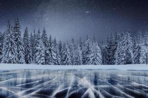 caminata de la estrella de lácteos por encima de los bosques de invierno. grietas en la superficie del hielo azul cerca de colinas de pinos. lago congelado en las montañas. los cárpatos ucrania europa foto