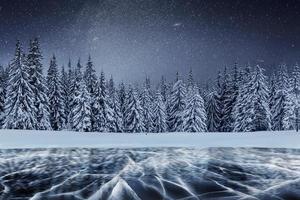 caminata de la estrella de lácteos por encima de los bosques de invierno. grietas en la superficie del hielo azul cerca de colinas de pinos. lago congelado en las montañas. los cárpatos ucrania europa foto