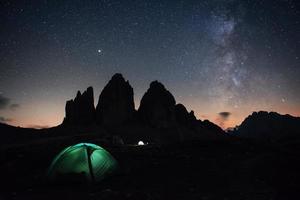 Our galaxy is on the sky. Two lighting tents with tourists inside near the Tre Cime three peaks mountains at night time