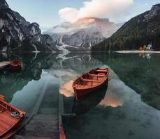 impresionante lugar para descansar. Barcos de madera en el lago de cristal con majestuosa montaña detrás. reflejo en el agua foto
