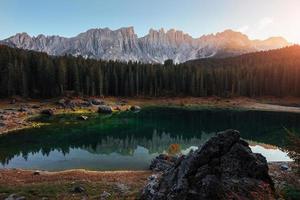 Plants are blooming in the water, you can see it by green color. Autumn landscape with clear lake, fir forest and majestic mountains photo