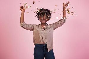 lanzando el confeti al aire. mujer afroamericana con fondo rosa detrás
