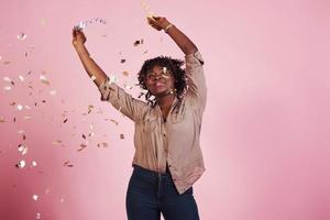 Joyful and happy. Throwing the confetti in the air. African american woman with pink background behind photo