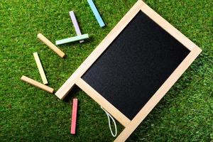 Top view of mini blackboard and colors on plastic grass background. Concept back to school photo