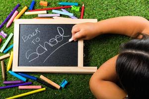 Back to school supplies arrangement vivid colorful on green grass and blackboard hand chalk photo