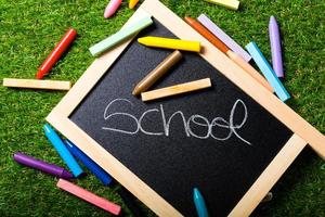 Top view of mini blackboard and colors on plastic grass background. Concept back to school photo