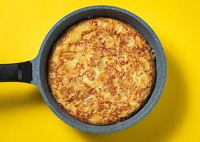 tortilla de patatas en sartén sobre fondo amarillo, plato típico español. foto