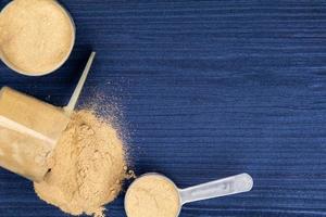 Scoops filled with protein powders on background blue wood photo
