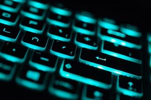 Closeup of laptop keyboard illumination, backlit keyboard. Aquamarine color light photo