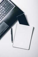 Modern white office desk table with laptop, smart phone and other supplies. Blank notebook page for input the text in the middle. Top view, flat lay. photo