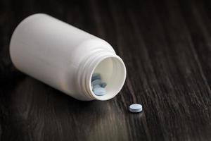 píldora de medicación en una fila sobre un fondo de madera. frasco de pastillas blanco foto