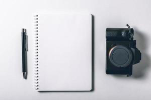 Modern white office desk table with pen and digital camera mirrorless. Blank notebook page for input the text in the middle. Top view, flat lay. photo
