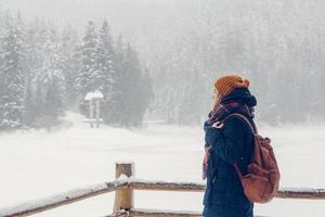 Portrait of a beautiful girl with a backpack on a background of snow-covered forest photo