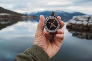 Beautiful male hand holds a magnetic compass against the background of the mountain and a lake photo