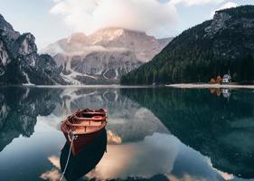 su luz del sol en la cima. barco de madera en el lago de cristal con majestuosa montaña detrás. reflejo en el agua. la capilla está en la costa derecha
