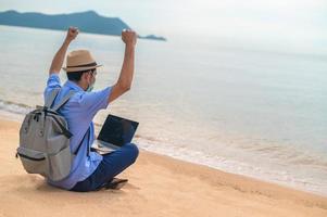 El hombre usa una máscara con un ordenador portátil en la playa, el mar y el hombre viajes vacaciones phuket sandbox Tailandia son la libertad financiera de la vida foto