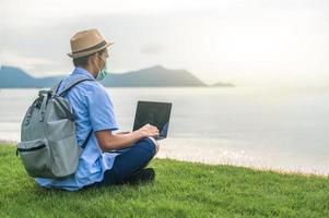 Man wear mask using laptop computer on beach  sea  and Man travel holiday Phuket sandbox Thailand are freedom life financial photo