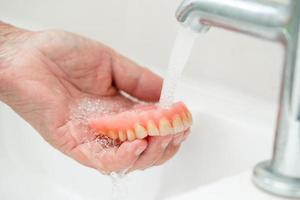 Paciente mujer mayor asiática sosteniendo y lavando la dentadura en la sala del hospital de enfermería foto