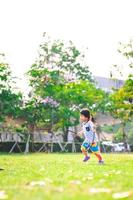 retrato de niña asiática está jugando peleas de acuerdo con su imaginación. en la mano del niño sostiene una vaina que contiene las semillas del árbol. niños corriendo sobre la hierba verde. imagen vertical. foto