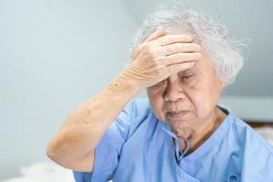 Asian senior or elderly old lady woman patient headache while sitting on bed in nursing hospital ward, healthy strong medical concept photo