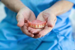 Asian senior or elderly old woman patient holding to use denture in nursing hospital ward, healthy strong medical concept photo