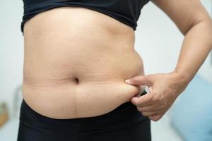 mujer asiática con sobrepeso muestra el vientre gordo en la oficina. foto