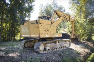 Excavadora con pala mecánica con orugas mientras excavaba en las tierras agrícolas de la langhe piamontesa foto