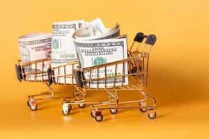 Shopping carts with dollars paper bills on a yellow background. Financial concept. photo