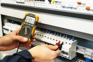 A male electrician who is testing the voltage in the switchboard photo