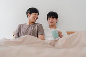 Asian Gay men couple talking having a great time at modern home. Young Asia lover male happy relax rest drink coffee after wake up while lying on bed in bedroom at house in the morning concept. photo