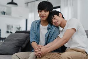 retrato joven pareja gay asiática sentirse feliz sonriendo en casa. los hombres asiáticos lgbtq relajan una sonrisa con dientes mirando a la cámara mientras están acostados en el sofá en la sala de estar en casa en el concepto de la mañana. foto