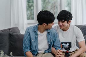 Young Asian gay couple influencer couple vlog at home. Teen korean LGBTQ men happy relax fun using camera record vlog video upload in social media while lying sofa in living room at house concept. photo