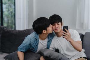 pareja gay influyente asiática vlog en casa. los hombres asiáticos lgbtq felices se relajan y se divierten usando la tecnología, el teléfono móvil, graba el estilo de vida, carga de video vlog en las redes sociales mientras está acostado en el sofá en el concepto de sala de estar. foto