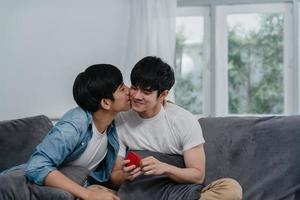 joven pareja gay asiática proponer en casa, hombres lgbtq coreanos adolescentes felices sonriendo tienen tiempo romántico mientras proponen y matrimonio sorpresa usan anillo de bodas en la sala de estar en el concepto de casa. foto