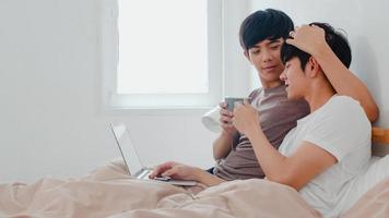 Pareja de hombres gay asiáticos usando computadora portátil y tomando café en casa moderna. Hombre joven amante de Asia feliz relajarse descansar juntos después de despertarse, viendo una película acostado en la cama en el dormitorio de la casa por la mañana foto
