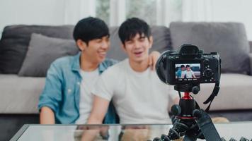 Young Asian gay couple influencer couple vlog at home. Teen korean LGBTQ men happy relax fun using camera record vlog video upload in social media while lying sofa in living room at house concept. photo