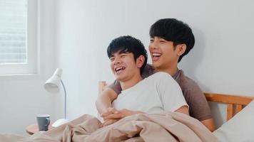 Handsome Asian gay couple talking on bed at home. Young Asian LGBTQ guy happy relax rest together spend romantic time after wake up in bedroom at modern house in the morning concept. photo