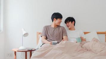 Asian Gay men couple talking having a great time at modern home. Young Asia lover LGBTQ male happy relax rest drink coffee after wake up while lying on bed in bedroom at house in the morning concept. photo