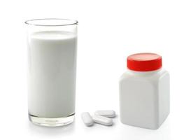 Frasco de pastillas y vaso de leche aislado sobre fondo blanco. foto