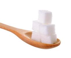 Cubitos de azúcares en una cuchara de madera aislado sobre fondo blanco. foto