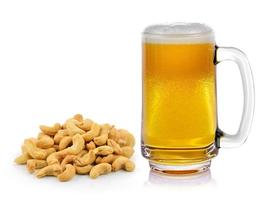 Mug fresh beer with cap of foam and cashew nuts heap on white background