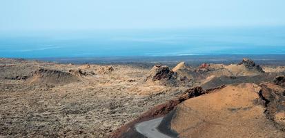Amazing landscape at Lanzarote. Road crossing a volcanic area with colorful soil and rocks. Horizon and ocean. Canary islands, Spain.