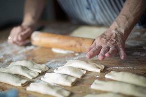 Typical asturian Christmas dessert. Aged woman's hands using a wooden roller pin to make casadielles filled with nuts. Homemade dough.Gastronomy photo